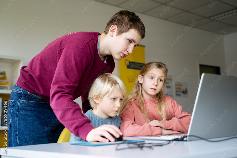 Teenage boy assisting students with coding in school classroom Teenage boy assisting students with coding in school classroom