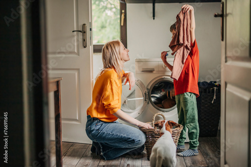 Son showing washed clothes to mother crouching near washing machine at home