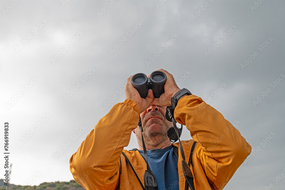 A man birdwatching with binoculars on a lake. A man birdwatching with binoculars on a lake.