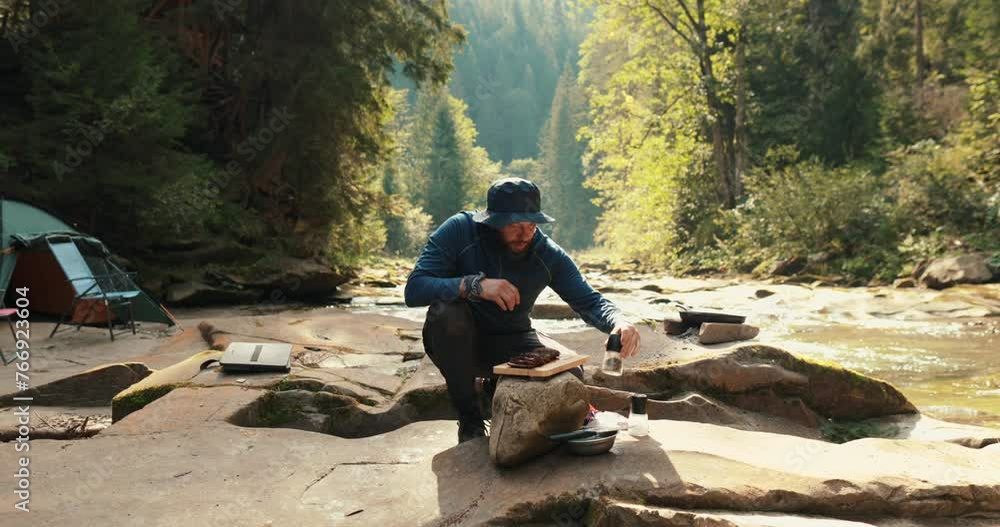Close-up of a lone tourist sitting on a stone in a tourist camp near a fire and chopping wood Close-up of a lone tourist sitting on a stone in a tourist camp near a fire and chopping wood