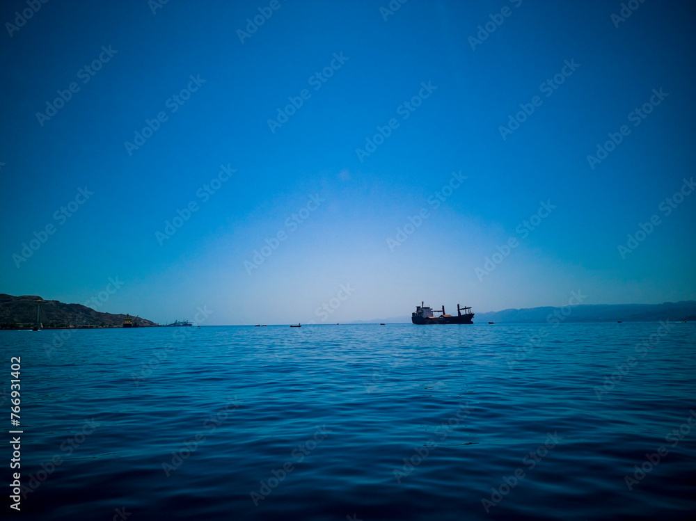 A photo of deep blue with a ship in the sea. The meeting of the sea and the sky in a blue hue. Horizontal photo. August 2022. Aqaba, Jordan