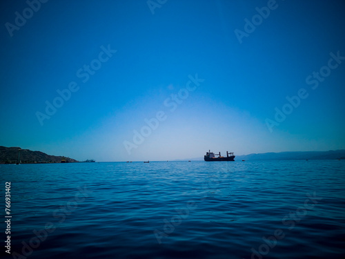 A photo of deep blue with a ship in the sea. The meeting of the sea and the sky in a blue hue. Horizontal photo. August 2022. Aqaba, Jordan