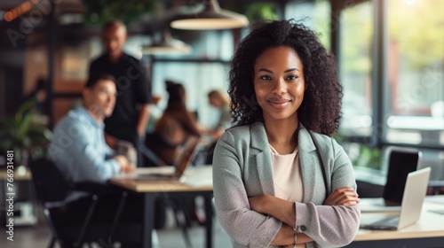 Portrait of young African American female looking camera standing arm crossed in front of colleagues running a business startup or new career path occupation, businesswoman lady lifestyle working photo
