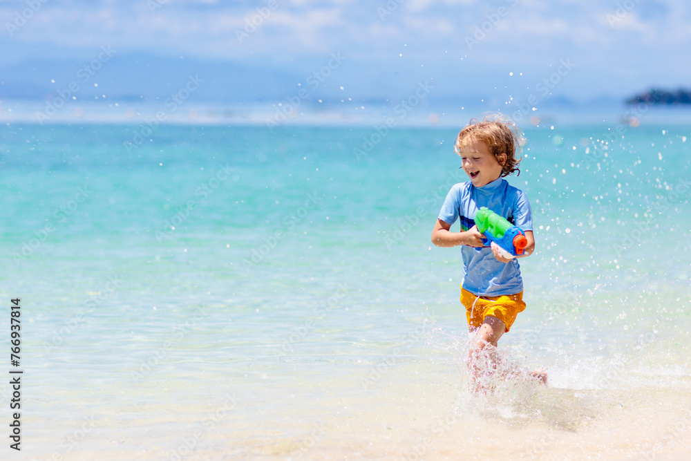 Child with toy water gun. Kids vacation beach fun.