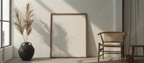 Sunlit mockup of an empty picture frame with a modern black organic-shaped vase holding dry festuca and bunny tail grass. photo