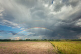 A rainbow in the cloudy sky over the rural fields