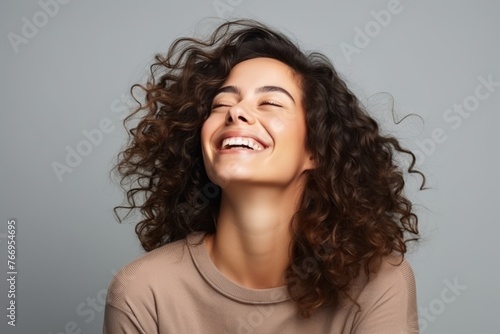 Portrait of a happy young woman with curly hair over gray background