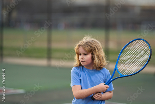 Cute Kid play tennis. Little kid hit tennis ball with tennis racket. Active exercise for kids. Summer activities for children. Child learning to play tennis. Sport Kid hitting Ball on court. © Volodymyr