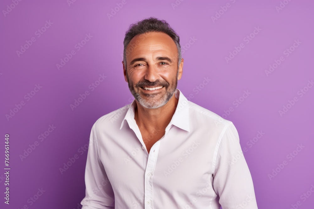 Handsome mature man in white shirt looking at camera and smiling while standing against purple background Handsome mature man in white shirt looking at camera and smiling while standing against purple background