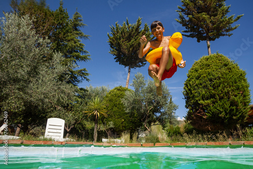 Teenager jumps with floatie into backyard pool on sunny day