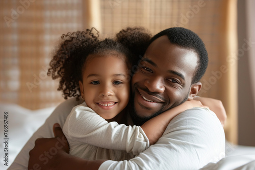 African American man and his little daughter hugging in bedroom