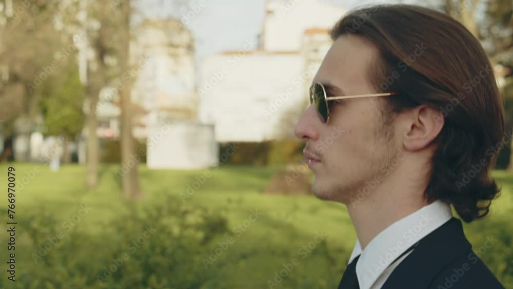 Young stylish man in business suit is walking on the street. Young Confident businessman walks in the city in a gold sunglasses. Stylish White man with brown hair is walking in the city on the summer Young stylish man in business suit is walking on the street. Young Confident businessman walks in the city in a gold sunglasses. Stylish White man with brown hair is walking in the city on the summer