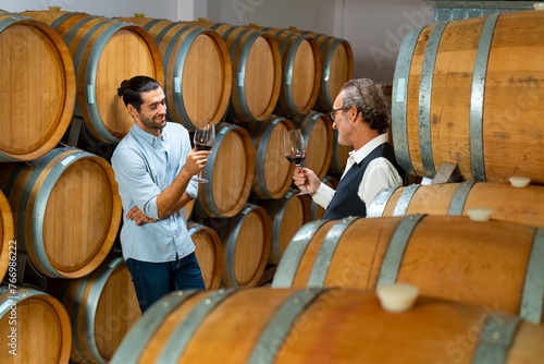 Professional Caucasian man sommelier tasting and sniffing red wine in wooden barrel at traditional wine cellar. Winery  brewery  liquor shop  wine factory manufacturing industry and winemaker concept.