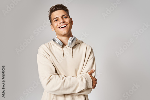 handsome young guy in headphones smiling with folded arms against light background © LIGHTFIELD STUDIOS