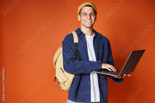 attractive student with backpack networking to laptop against terracotta background
