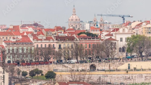 Aerial view over the center of Lisbon to the viewpoint called Miradouro de Sao Pedro de Alcantara timelapse. Colorful houses on a hill. Dome of Estrela basilica church. People in the park. Portugal photo