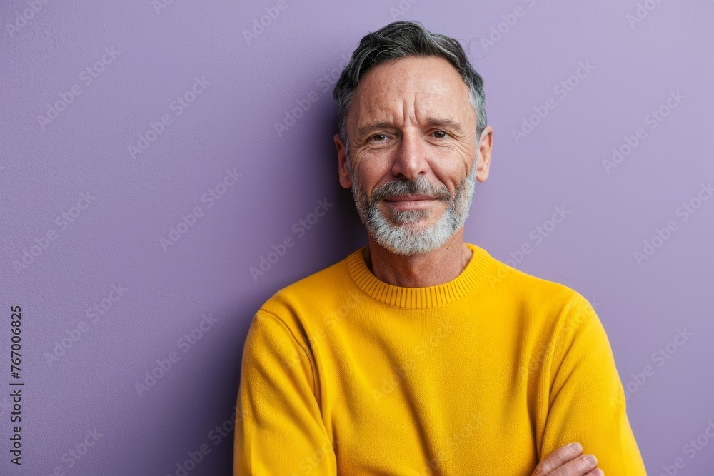 Portrait of handsome senior man with grey beard in yellow sweater standing against purple background Portrait of handsome senior man with grey beard in yellow sweater standing against purple background