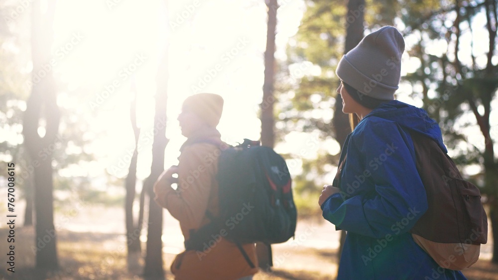 Obraz premium two hiker work as a team. with backpacks walking in winter in a forest park in the sunny glare at sunset. Two tourists sun travel hiking in forest park, overcoming difficulties, teamwork concept