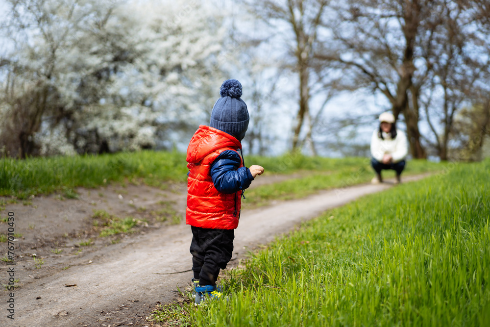 Small child walks along path with his mother in the spring Small child walks along path with his mother in the spring
