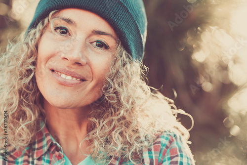 Middle age beautiful woman portrait with hipster style and warm woolen hat in outdoor with defocused bokeh nature background - cheerful happy people female caucasian looking at camera © simona