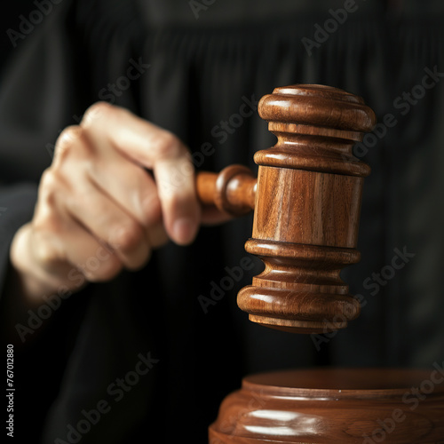 A judge is holding a gavel and wearing a black robe. The gavel is wooden and has a black handle