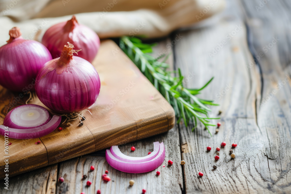 Three red onions are on a wooden cutting board. The onions are cut in half and are surrounded by pepper and herbs