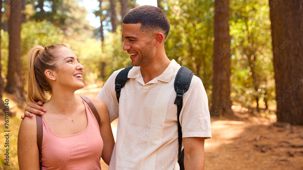 Portrait Of Couple Wearing Backpacks Hiking Along Trail Through Countryside