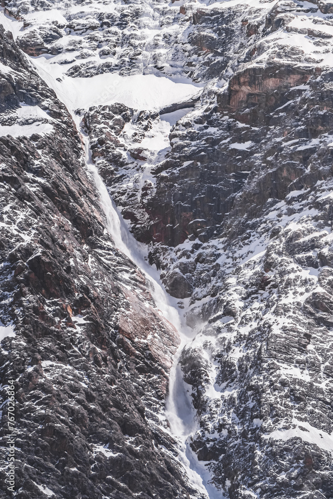 A snow avalanche comes down from the rocky Fan Mountains in Tajikistan, pieces of snow fall like snowfall along a cascade of rocks A snow avalanche comes down from the rocky Fan Mountains in Tajikistan, pieces of snow fall like snowfall along a cascade of rocks
