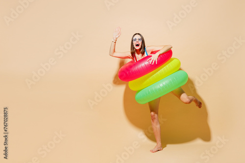 Full body young woman wear one-piece swimsuit glasses near hotel pool hold rubber ring look camera waving hand isolated on plain pastel light beige background Summer vacation sea rest sun tan concept