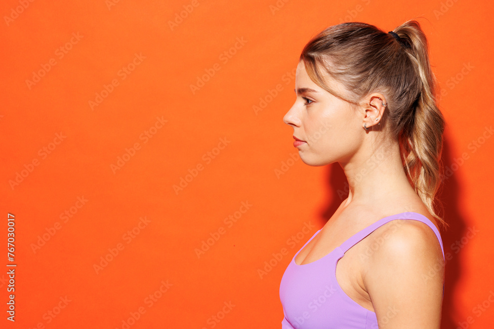 Close up side view young fitness trainer instructor sporty woman sportsman wear purple top clothes spend time in home gym look aside isolated on plain orange background. Workout sport fit abs concept. Close up side view young fitness trainer instructor sporty woman sportsman wear purple top clothes spend time in home gym look aside isolated on plain orange background. Workout sport fit abs concept.