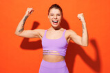 Young fitness trainer instructor sporty woman sportsman wear purple top clothes spend time in home gym do winner gesture clench fist isolated on plain orange background. Workout sport fit abs concept