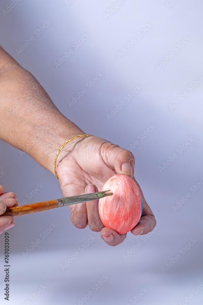 Hand of an indian woman holding an Easter egg and painting with a paintbrush on a white background. closeup Hand of an indian woman holding an Easter egg and painting with a paintbrush on a white background. closeup