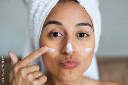 Playful woman applying moisturizer on her face photo