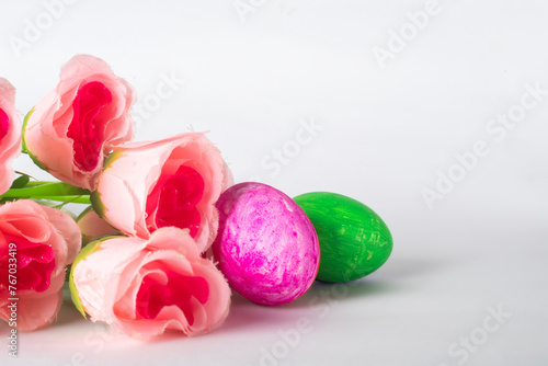 Easter eggs and pink rose flowers on a white background with space for text.
