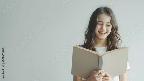 A happy white girl is reading a beige book and laughing on a plain white background with copy-space for text. photo