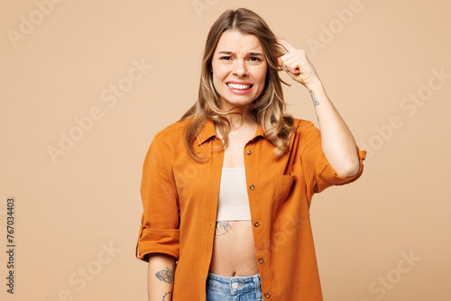 Young shocked mistaken sad Caucasian woman wear orange shirt casual clothes look camera hold scratch head look camera isolated on plain pastel light beige background studio portrait Lifestyle concept