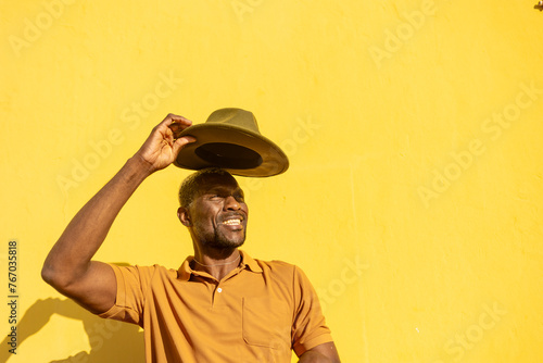 Smiling man tipping his hat against a yellow wall photo