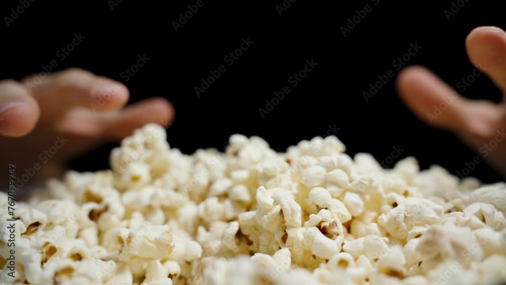 Hands appear from darkness on both sides and take handfuls of popcorn. Close-up, slow motion.