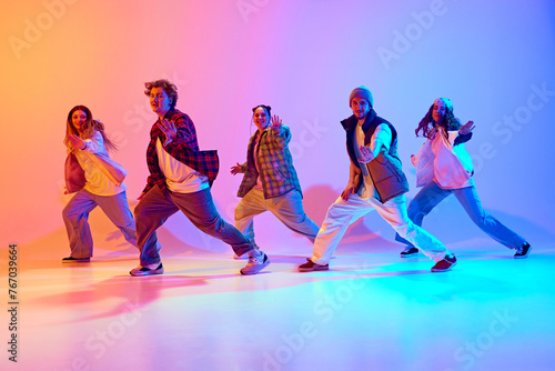 Positive young people, men and women in sport style clothes dancing contemporary dance styles over gradient studio background in neon. Concept of modern dance, hobby, active lifestyle, youth culture