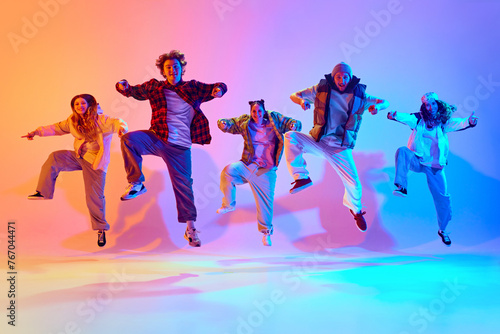 Dynamic poses in dancing. Young people, friends performing hip hop against gradient studio background in neon light. Concept of modern dance style, hobby, active lifestyle, youth culture