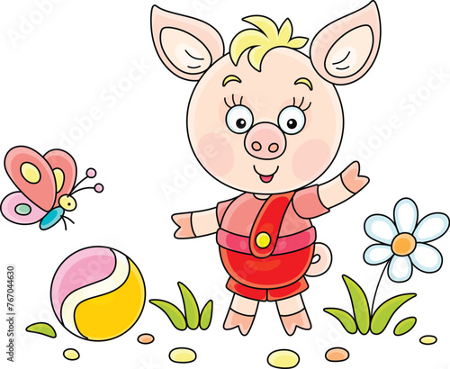 Funny cartoony little piglet playing with its ball and merry butterfly on a green summer lawn, vector cartoon illustration on a white background