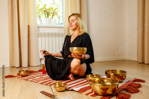 Woman playing on a tibetian singing bowl in cozy room meditating in a yoga