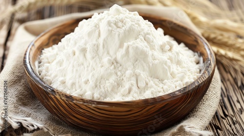 White flour in a wooden bowl on a rustic table. The flour is piled high in the bowl and is surrounded by wheat. photo