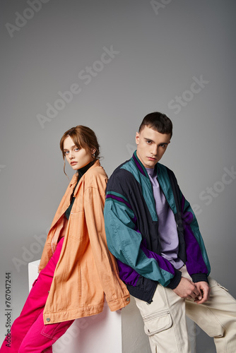 caring appealing couple in vivid stylish bombers looking at camera on gray backdrop on white cube