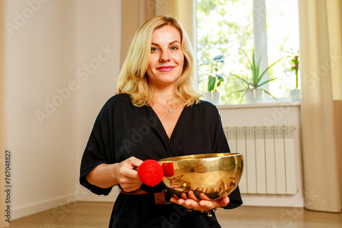 Woman playing on a tibetian singing bowl in cozy room meditating in a yoga