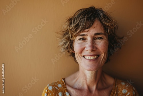 Portrait of smiling middle aged woman with curly hair against beige wall