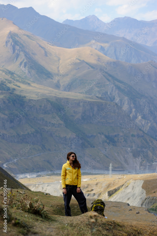 Standing woman hiker in yellow jacket and sunglasses in high mountains 