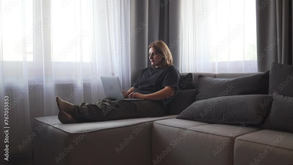 Happy young caucasian woman using texting mobile phone or chat and smiling with laptop computer sitting of the sofa in home. Communication female looking message at cell phone or smartphone. Slow Happy young caucasian woman using texting mobile phone or chat and smiling with laptop computer sitting of the sofa in home. Communication female looking message at cell phone or smartphone. Slow