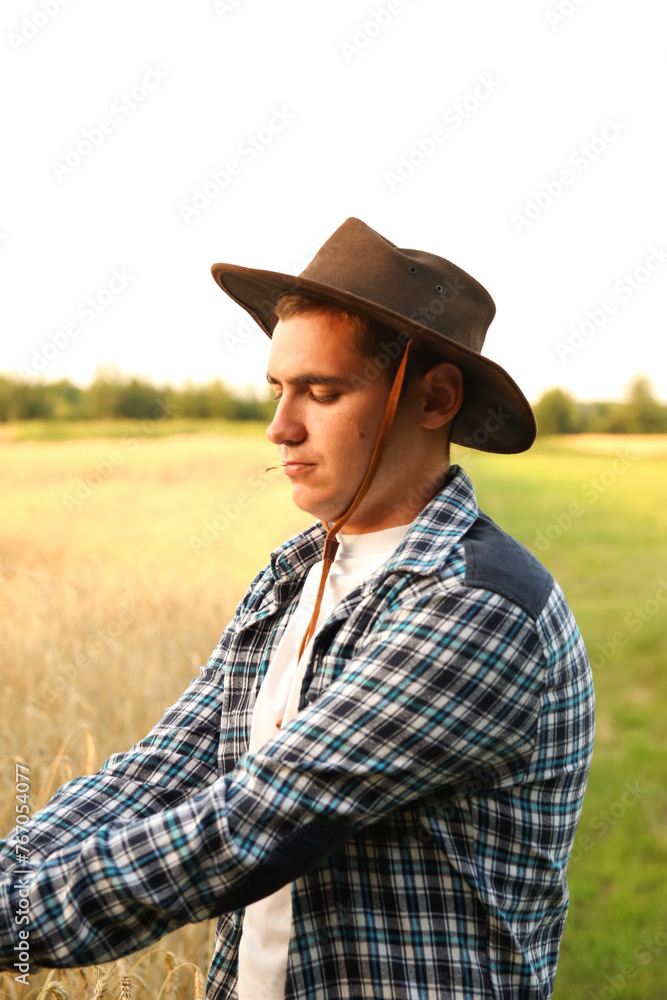 A cheerful portrait of a young cowboy-farmer. Vertical. Profile. expertise and dedication to agriculture, with a blurred agricultural landscape in the background