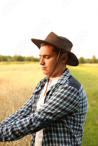 A cheerful portrait of a young cowboy-farmer. Vertical. Profile. expertise and dedication to agriculture  with a blurred agricultural landscape in the background